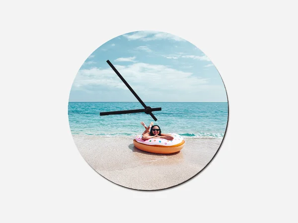 Die runde Wanduhr mit Foto zeigt ein Kind im Schwimmring am Strand vor dem Meer und kombiniert Uhrzeit mit Urlaubsstimmung.